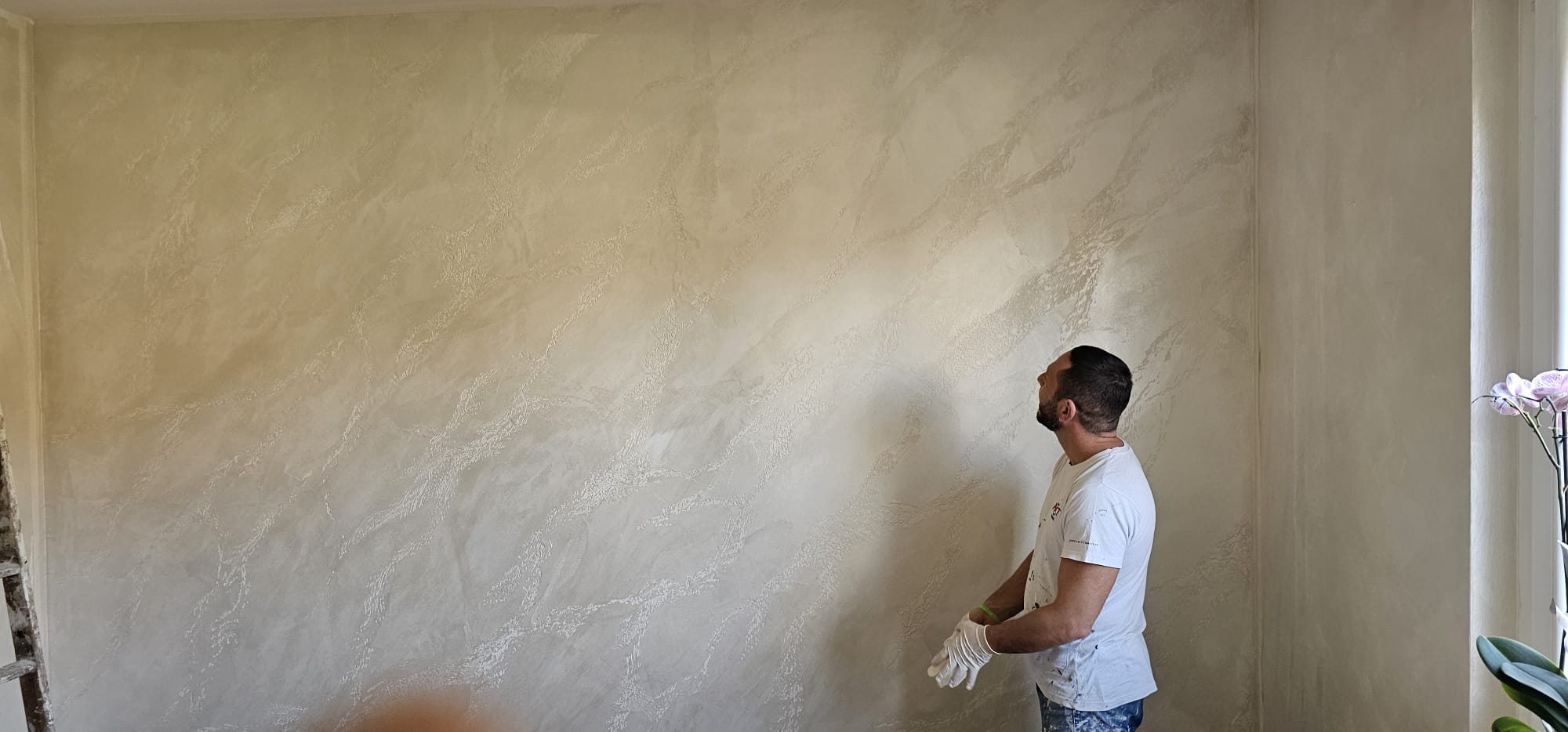 Salvatore Pollara, decoratore d'interni a Torino, accanto a una parete a finitura materica appena realizzata